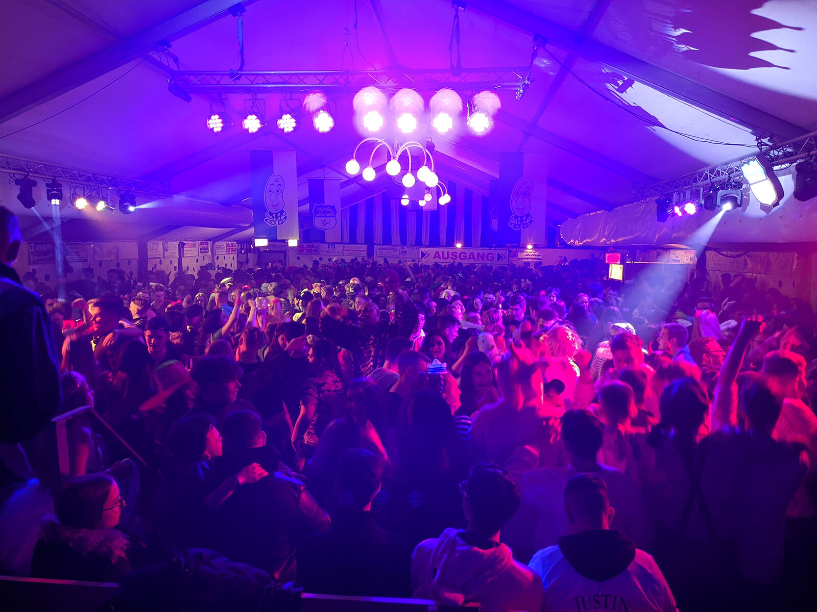 Packed festival tent dance floor in purple light